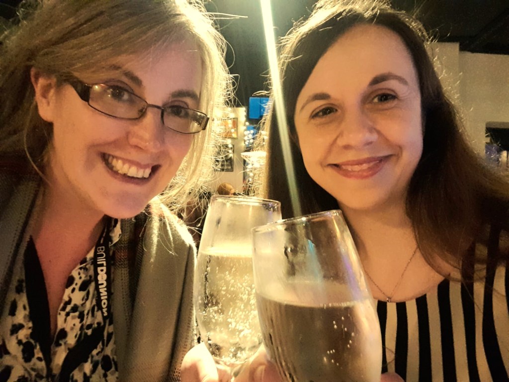 Two women smiling in close proximity and toasting glasses of prosecco