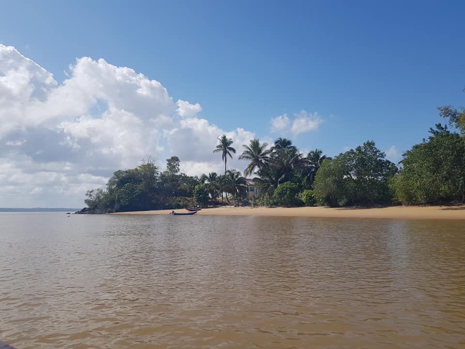 WIde river, and river bank with tropical trees and bushes, and some small boats by the shore